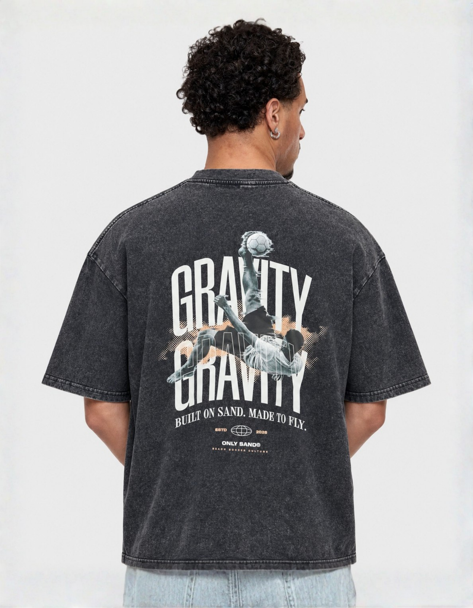 Back view of the GRAVITY washed charcoal-black T-shirt with an overhead-kick graphic and BUILT ON SAND. MADE TO FLY. slogan.